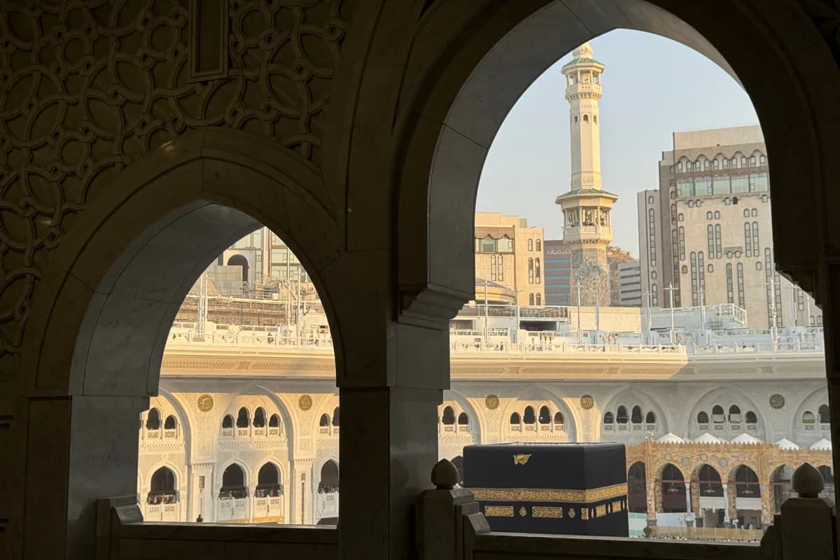 The Kaaba and a minaret framed by carved stone arches inside the Masjid al-Haram