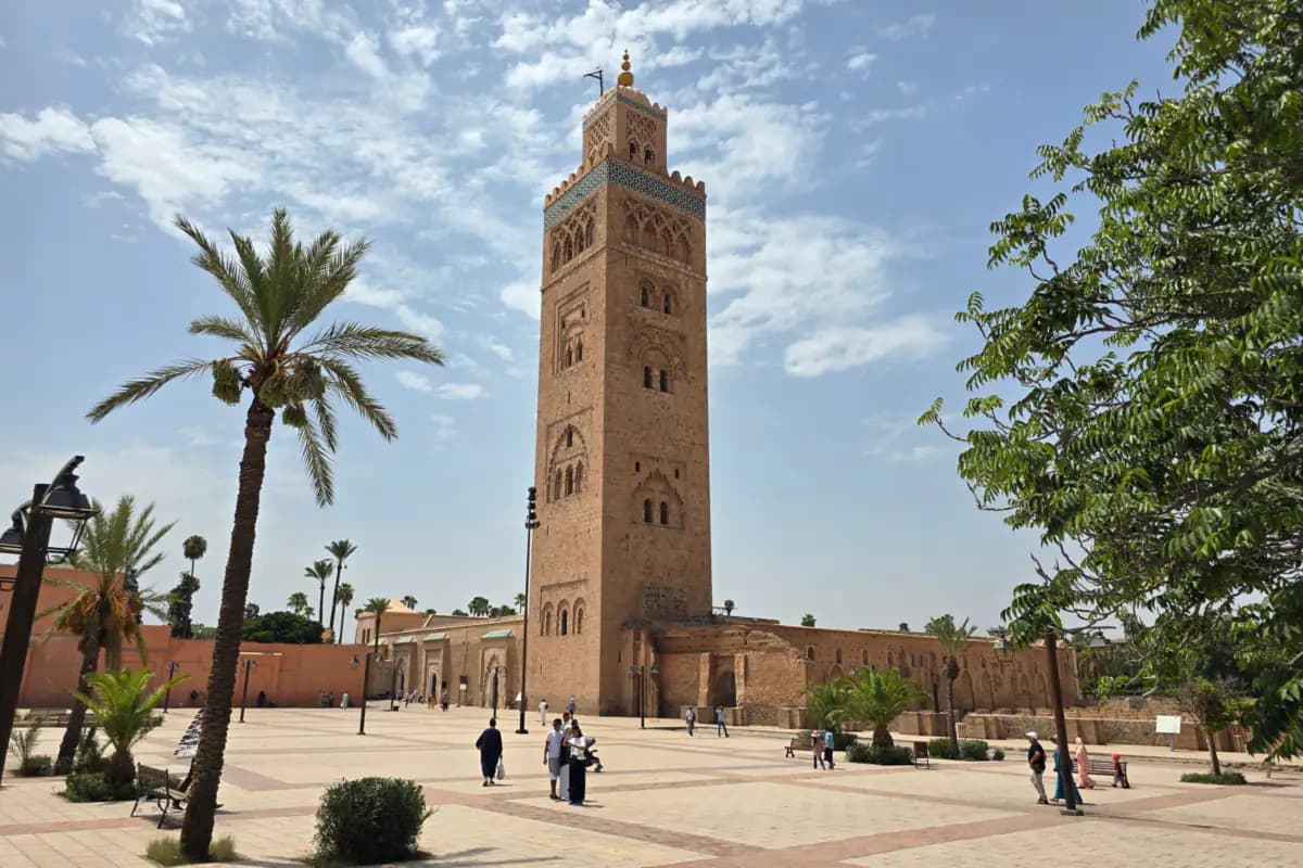 The Koutoubia Mosque minaret rising above palm trees and a paved square in Marrakech