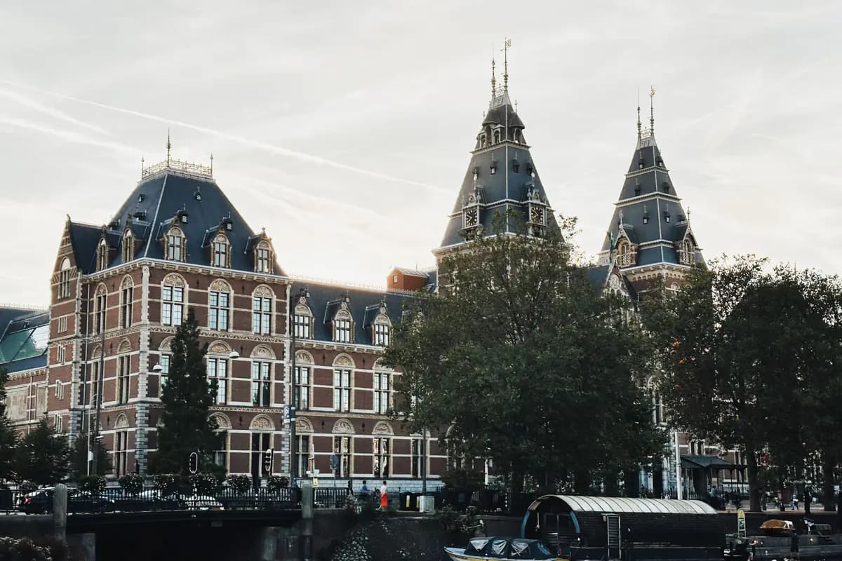 The red brick Rijksmuseum in Amsterdam, with its towers and slate roofs, seen across a canal with moored boats
