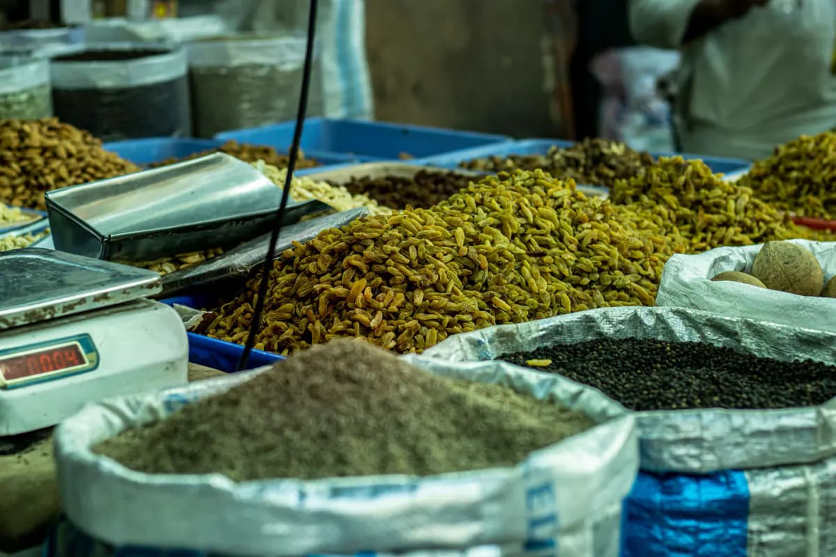 Sacks and trays of raisins, ground spice, black peppercorns and other dried goods beside a scale at a market stall
